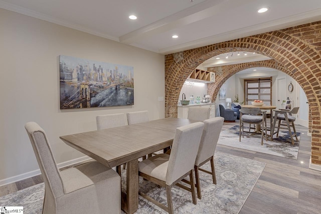 dining space featuring ornamental molding, wood finished floors, arched walkways, and baseboards