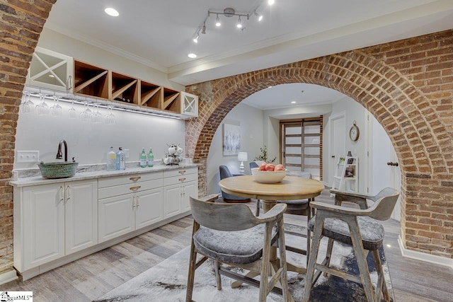 dining area with arched walkways, brick wall, crown molding, and light wood-style floors