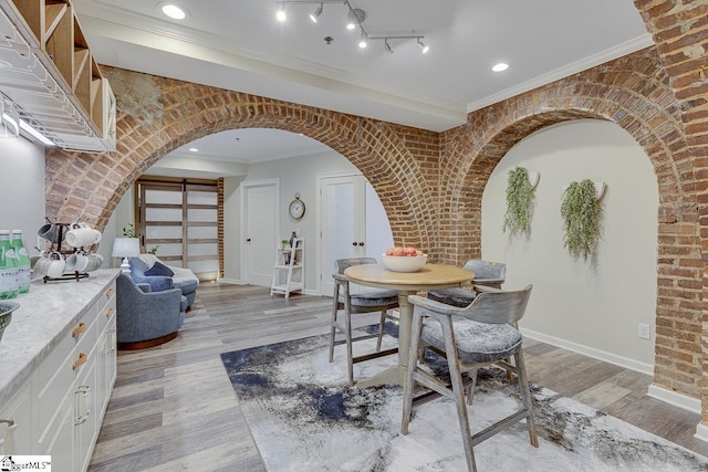 dining area featuring baseboards, arched walkways, ornamental molding, and light wood finished floors