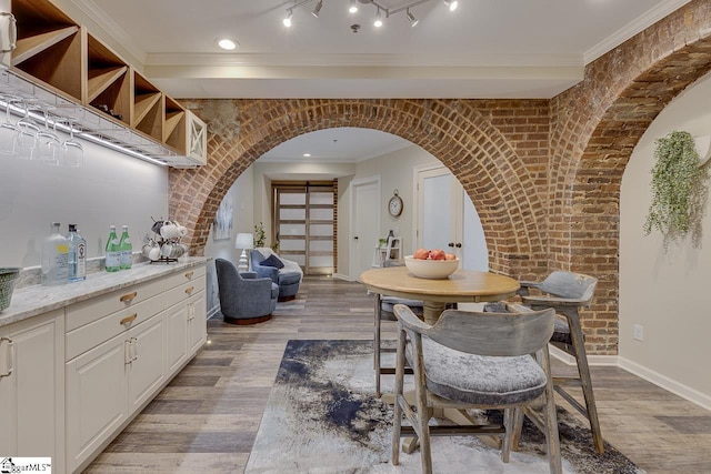 dining area featuring light wood-style flooring, ornamental molding, arched walkways, brick wall, and baseboards