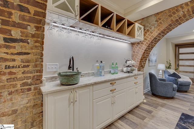 bar featuring light wood finished floors, brick wall, crown molding, and arched walkways