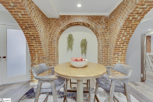 dining room with recessed lighting, wood finished floors, brick wall, and ornamental molding