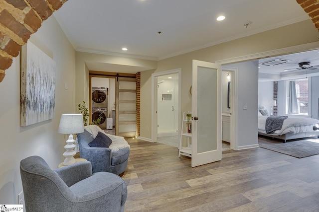 living area featuring light wood-style flooring, stacked washer and clothes dryer, and crown molding