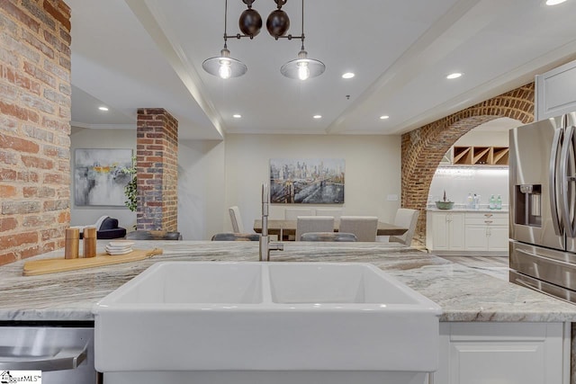 kitchen featuring brick wall, light stone counters, white cabinets, stainless steel appliances, and a sink