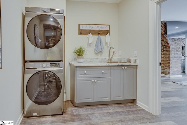 clothes washing area with baseboards, light wood-type flooring, cabinet space, stacked washer / drying machine, and a sink