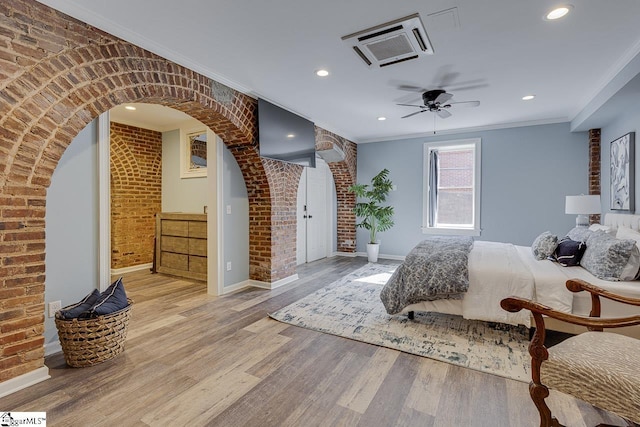 bedroom with wood finished floors, arched walkways, brick wall, crown molding, and baseboards