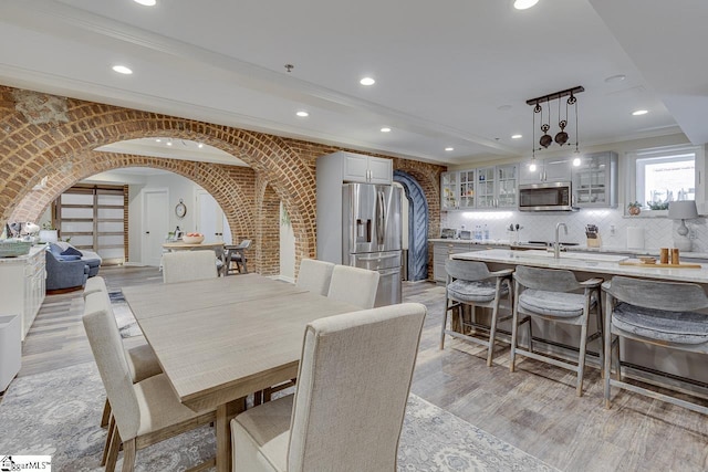 dining space featuring arched walkways, light wood finished floors, brick wall, and crown molding