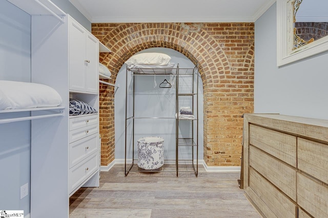 interior space with brick wall, crown molding, baseboards, walk in shower, and wood finished floors