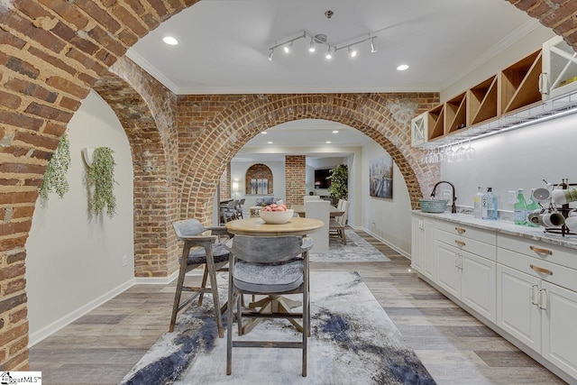 unfurnished dining area with brick wall, baseboards, light wood-style floors, and ornamental molding