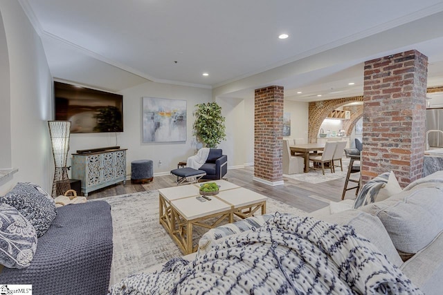 living area featuring ornamental molding, recessed lighting, wood finished floors, arched walkways, and ornate columns