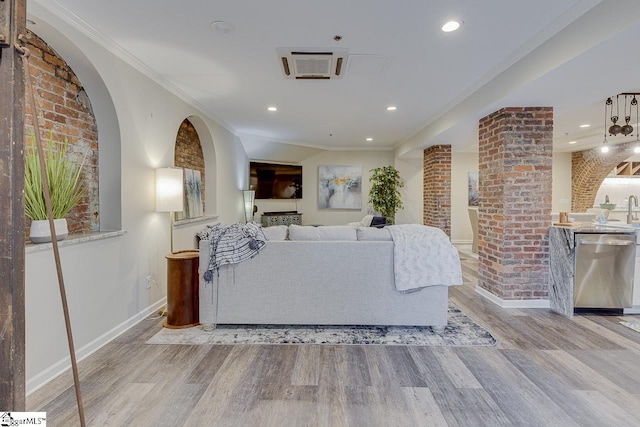 living room featuring brick wall, crown molding, baseboards, recessed lighting, and wood finished floors