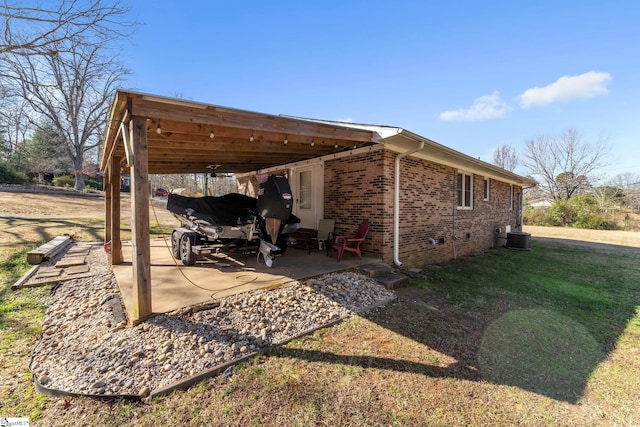 exterior space featuring a lawn, cooling unit, an attached carport, brick siding, and a patio area