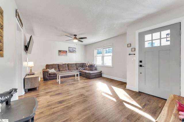 living area with baseboards, a ceiling fan, and light wood finished floors