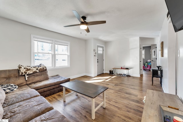 living room with baseboards, a textured ceiling, wood finished floors, and a ceiling fan