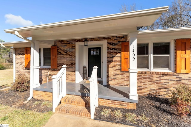 doorway to property featuring a porch and brick siding