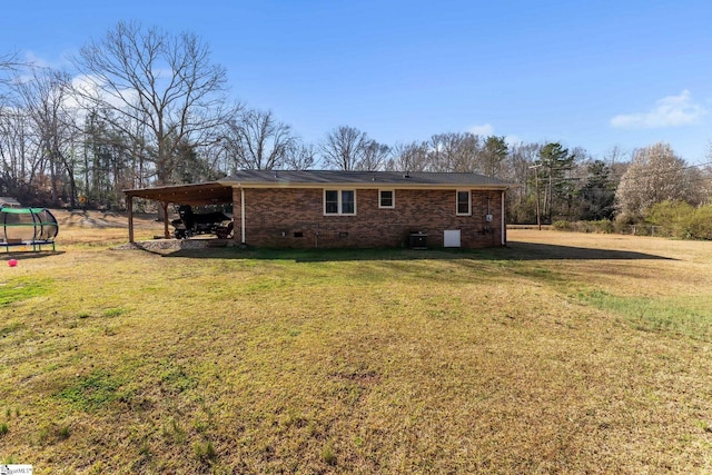 view of side of home with a carport, crawl space, a trampoline, a lawn, and brick siding