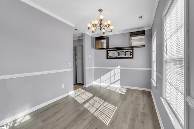 unfurnished dining area with an inviting chandelier, wood finished floors, crown molding, and baseboards