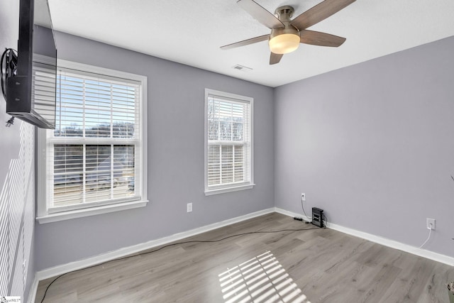 unfurnished room with a ceiling fan, wood finished floors, baseboards, and visible vents