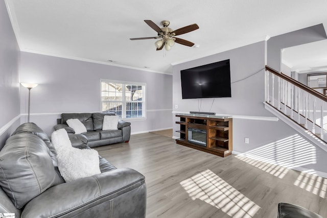 living area featuring stairway, wood finished floors, a ceiling fan, baseboards, and ornamental molding