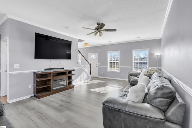 living room featuring crown molding, baseboards, ceiling fan, stairway, and wood finished floors