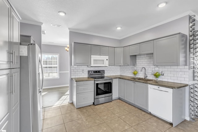 kitchen featuring dark countertops, gray cabinetry, ornamental molding, appliances with stainless steel finishes, and a sink