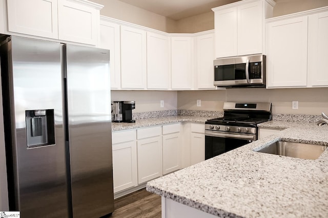 kitchen featuring a sink, light stone counters, wood finished floors, white cabinetry, and stainless steel appliances