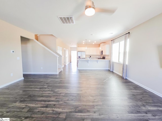 unfurnished living room with visible vents, a ceiling fan, dark wood-style floors, baseboards, and stairs