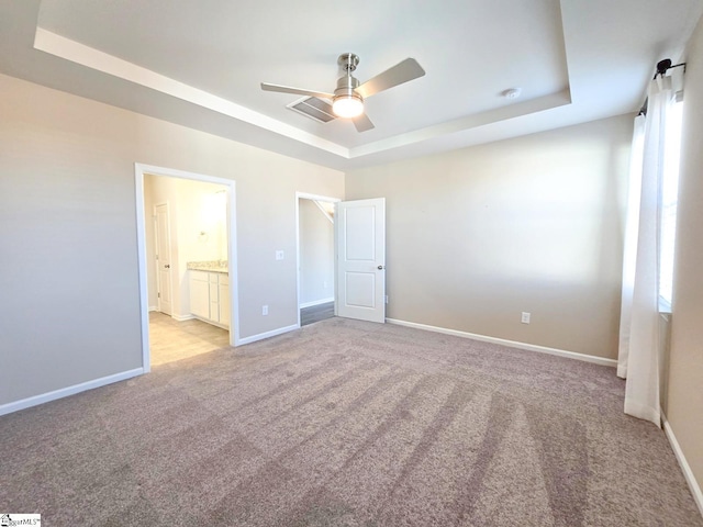 unfurnished bedroom featuring ensuite bath, a tray ceiling, baseboards, and light carpet