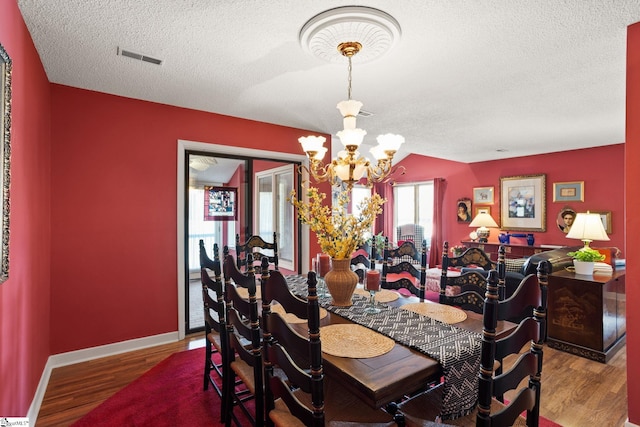 dining room featuring wood finished floors, visible vents, baseboards, an inviting chandelier, and a textured ceiling