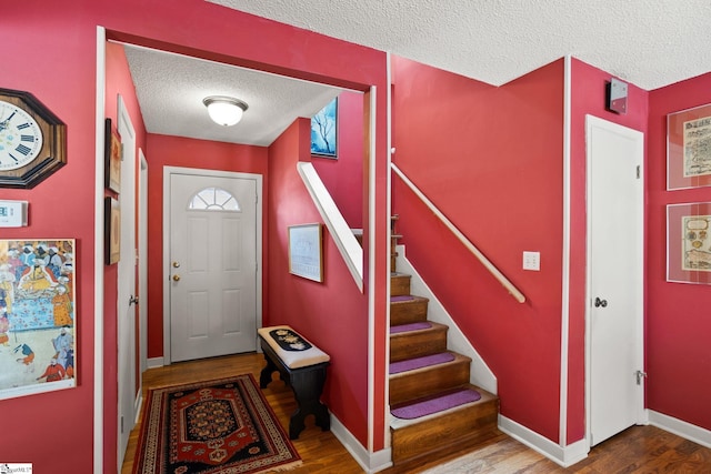 foyer with baseboards, a textured ceiling, wood finished floors, and stairs