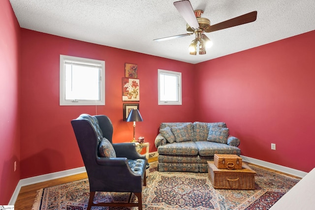 living room with baseboards, a textured ceiling, wood finished floors, and a ceiling fan