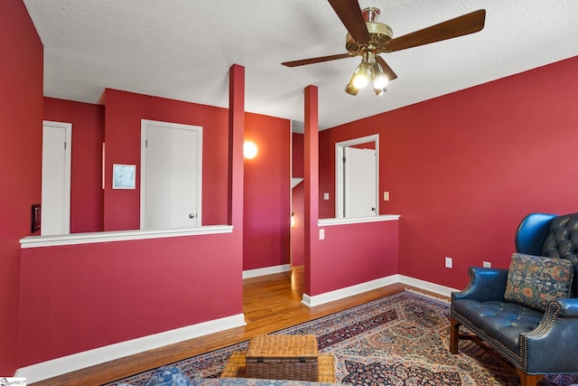 living area featuring a textured ceiling, baseboards, ceiling fan, and wood finished floors