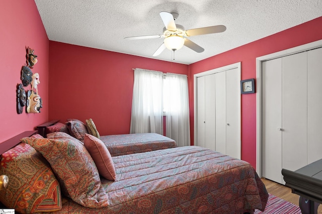 bedroom featuring multiple closets, a textured ceiling, wood finished floors, and a ceiling fan