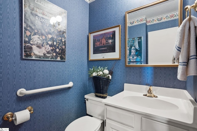 half bath featuring toilet, vanity, and wallpapered walls