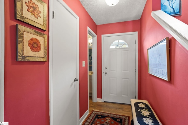 doorway to outside featuring a textured ceiling, baseboards, and wood finished floors