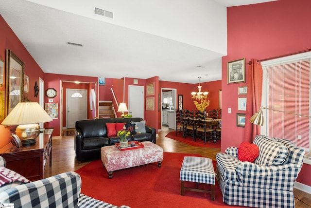 living room featuring visible vents, baseboards, a chandelier, stairway, and wood finished floors