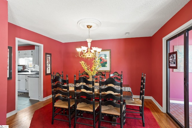 dining area featuring a notable chandelier, wood finished floors, baseboards, and a textured ceiling