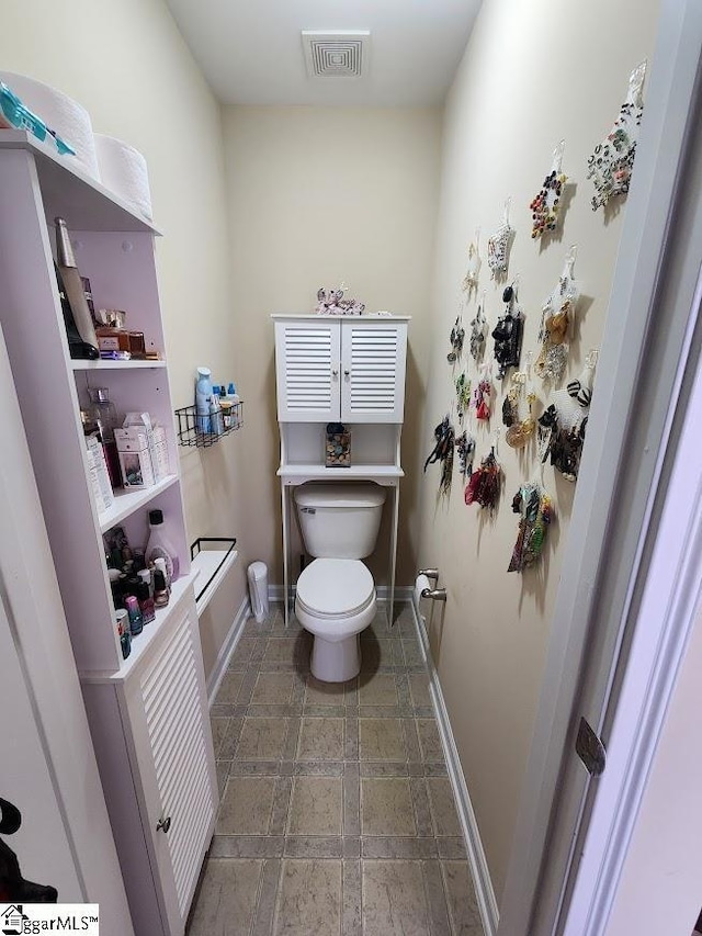 bathroom featuring stone tile flooring, visible vents, toilet, and baseboards