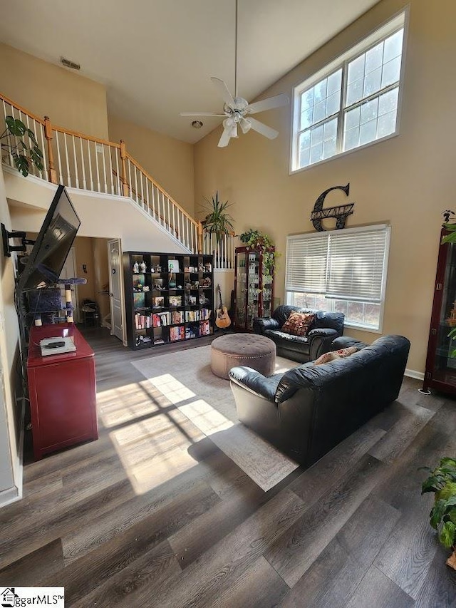 living area with wood finished floors, baseboards, visible vents, ceiling fan, and a towering ceiling