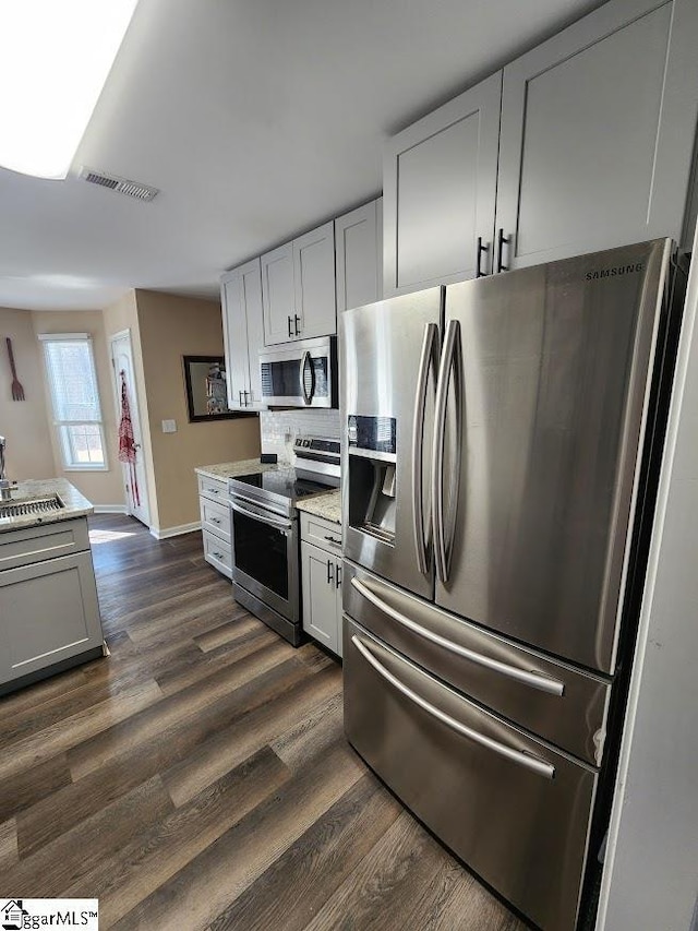 kitchen featuring visible vents, light stone countertops, appliances with stainless steel finishes, and dark wood-style flooring