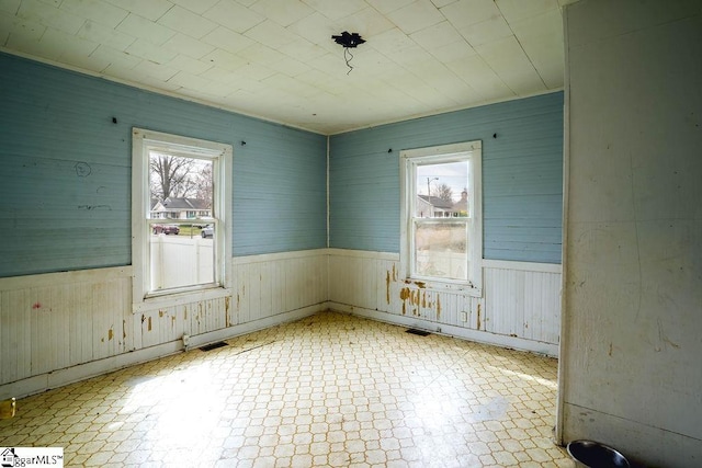 spare room featuring tile patterned floors, a healthy amount of sunlight, and wainscoting