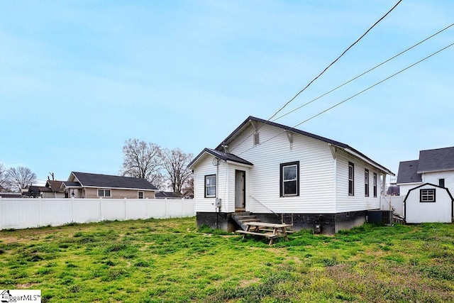 rear view of house featuring an outbuilding, a lawn, entry steps, a shed, and fence