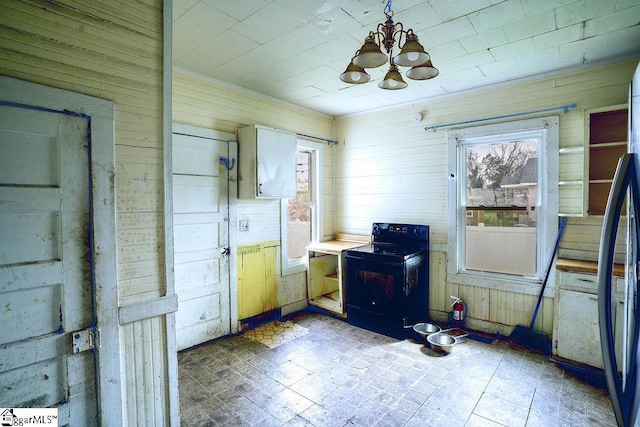 kitchen featuring wooden walls, an inviting chandelier, freestanding refrigerator, black range with electric cooktop, and decorative light fixtures