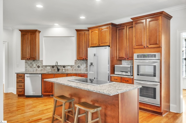 kitchen featuring light wood-style flooring, ornamental molding, a sink, appliances with stainless steel finishes, and a kitchen bar