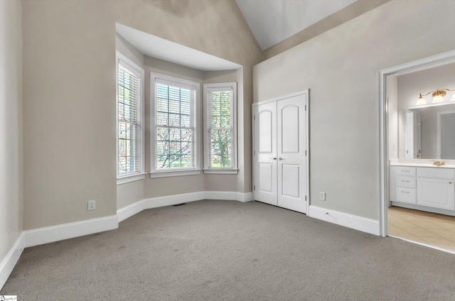 unfurnished bedroom with baseboards, ensuite bath, vaulted ceiling, a closet, and light colored carpet