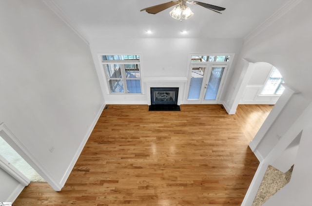 living area featuring light wood finished floors, baseboards, ceiling fan, a fireplace with flush hearth, and ornamental molding