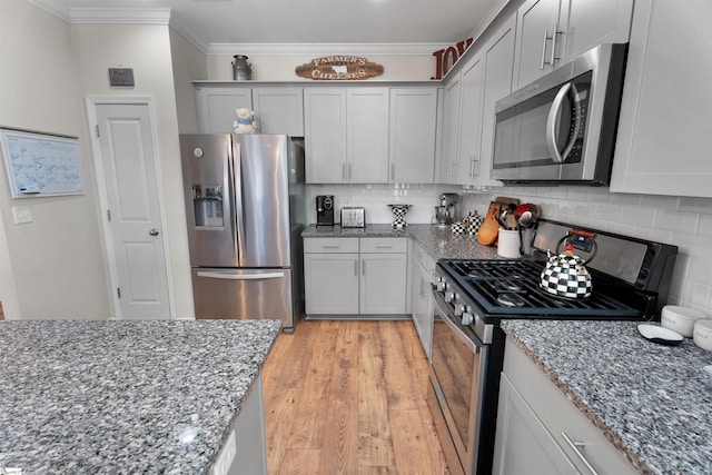 kitchen featuring light stone countertops, light wood finished floors, ornamental molding, decorative backsplash, and appliances with stainless steel finishes