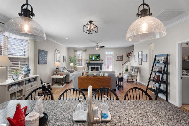 dining space with wood finished floors, a ceiling fan, baseboards, a warm lit fireplace, and crown molding