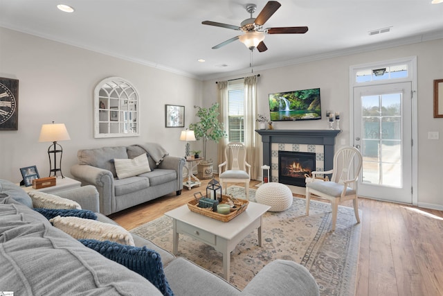 living area with a ceiling fan, visible vents, ornamental molding, wood-type flooring, and a tiled fireplace