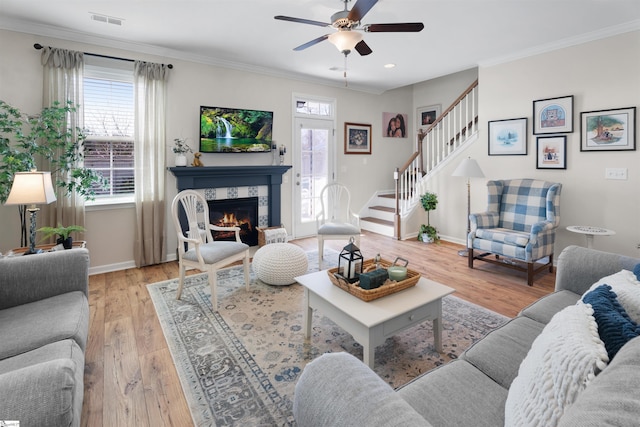 living room featuring light wood finished floors, visible vents, stairs, ornamental molding, and a ceiling fan